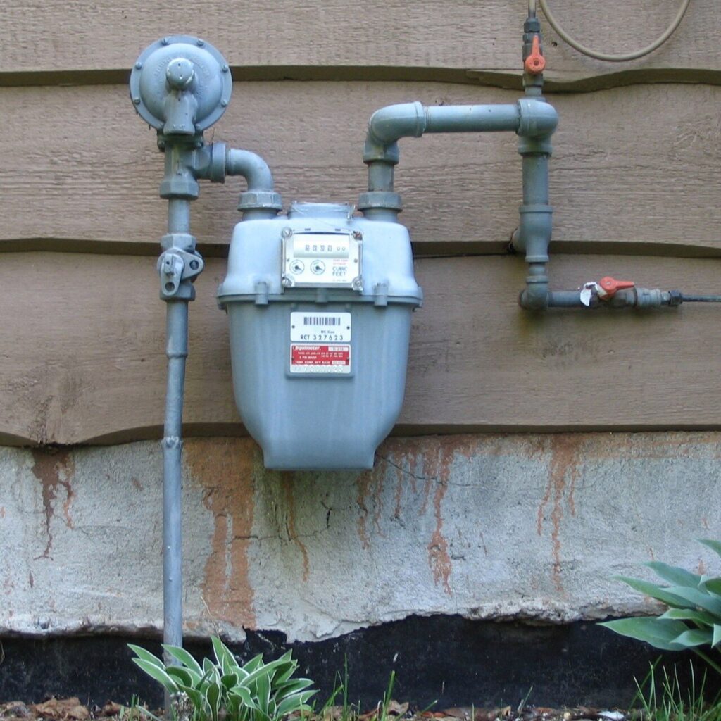 A residential natural gas meter and riser piping mounted on a home's siding